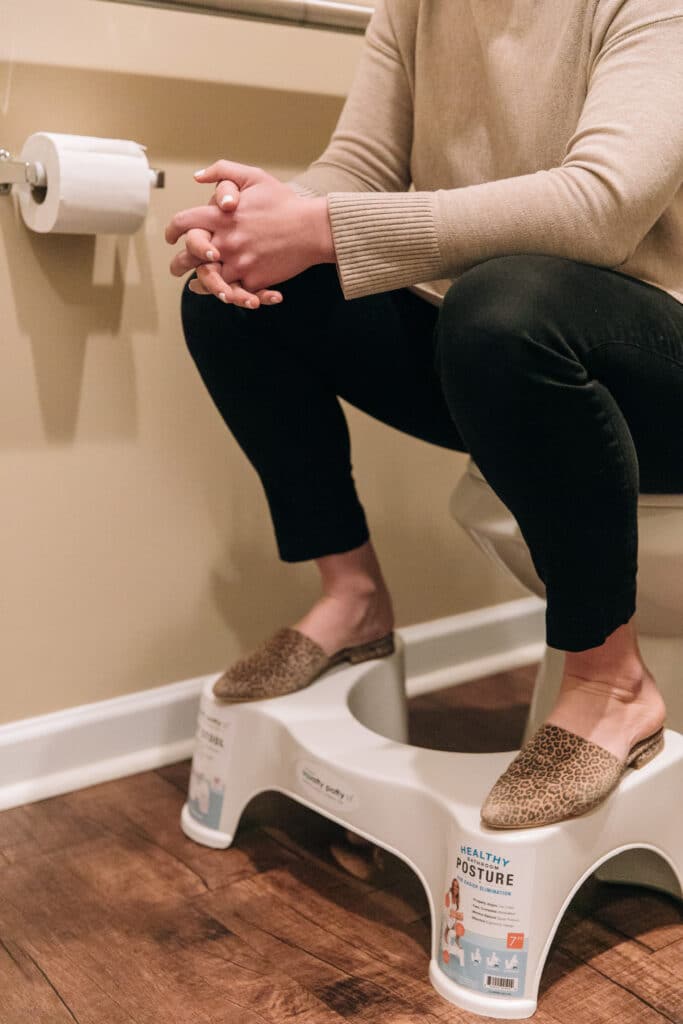 female seated on toilet with feet on stool